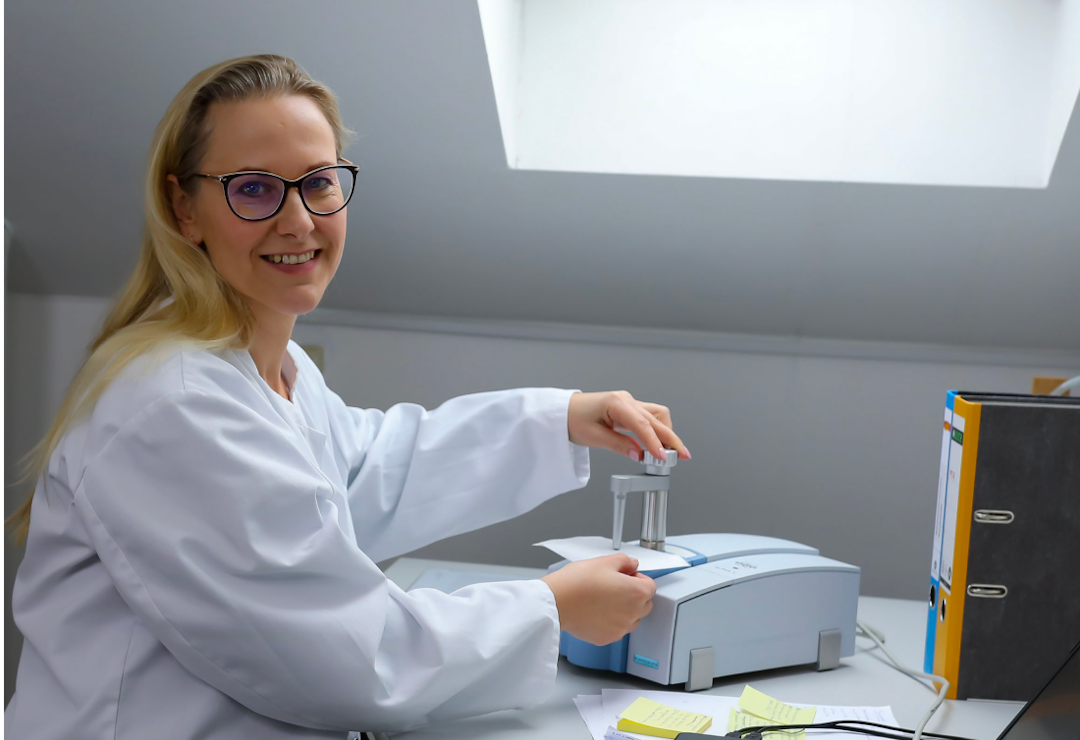 Frau im Laborkittel sitzt vor einem FTIR-Gerät