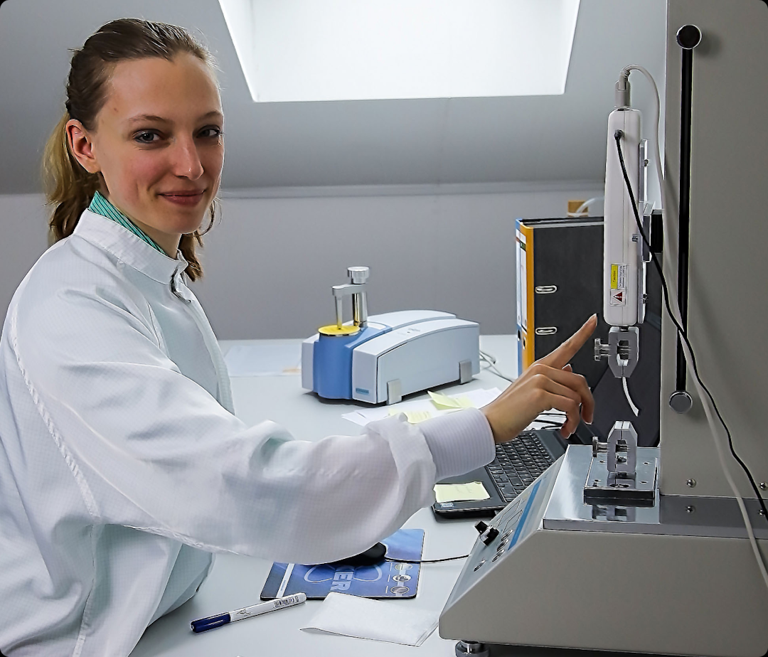 Woman wearing a white lab coat, operating a machine for seam strength tests.